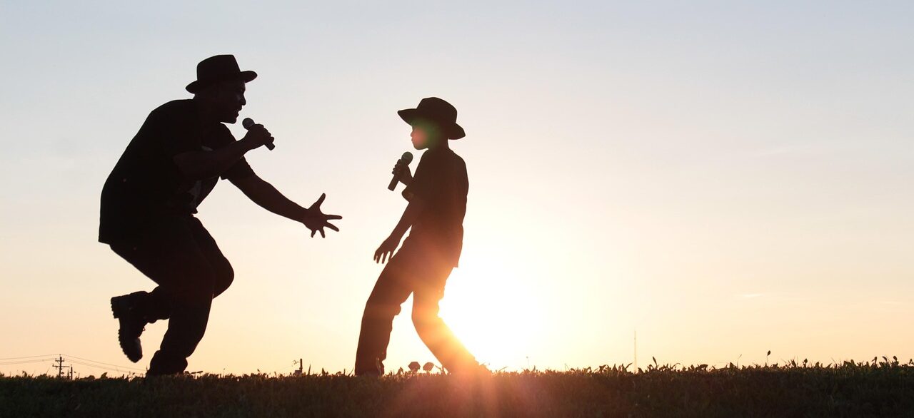 Vater und Sohn singen vor einem Sonnenuntergang.