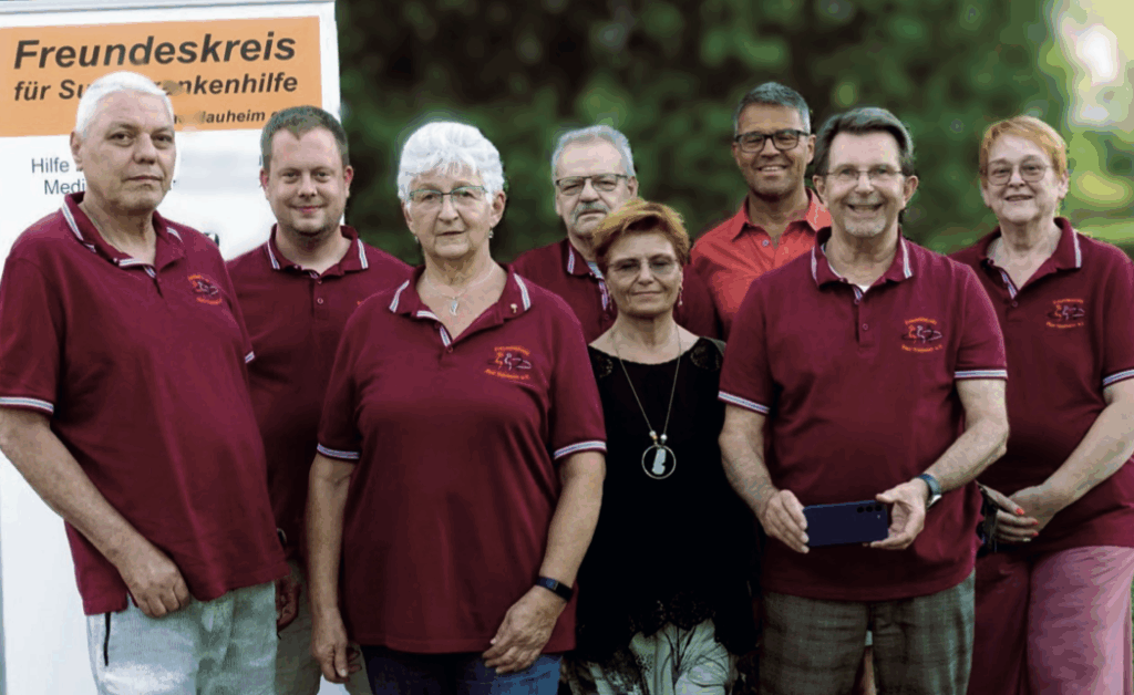 Es ist eine große Gruppe von Menschen zu sehen, die rote Polos tragen mit einem Banner mit der Aufschrift "Freundeskreis für Suchtkrankenhilfe" daraufstehend.