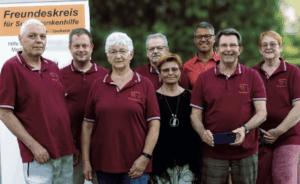 Es ist eine große Gruppe von Menschen zu sehen, die rote Polos tragen mit einem Banner mit der Aufschrift "Freundeskreis für Suchtkrankenhilfe" daraufstehend.