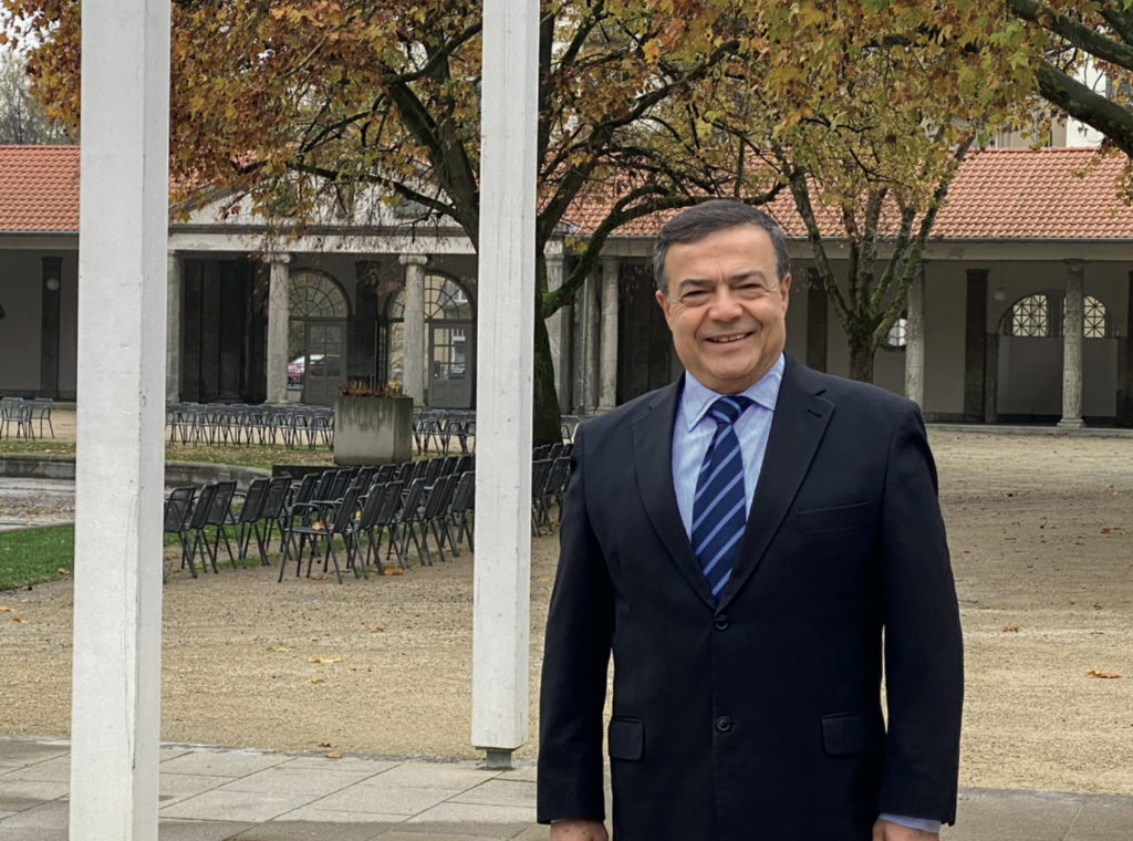 Mann mit dunklen Haaren, schwarzem Anzug und blauer Krawatte