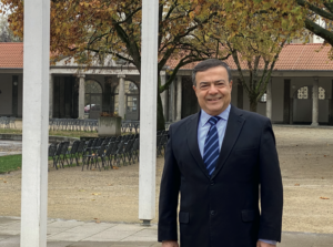 Mann mit dunklen Haaren, schwarzem Anzug und blauer Krawatte